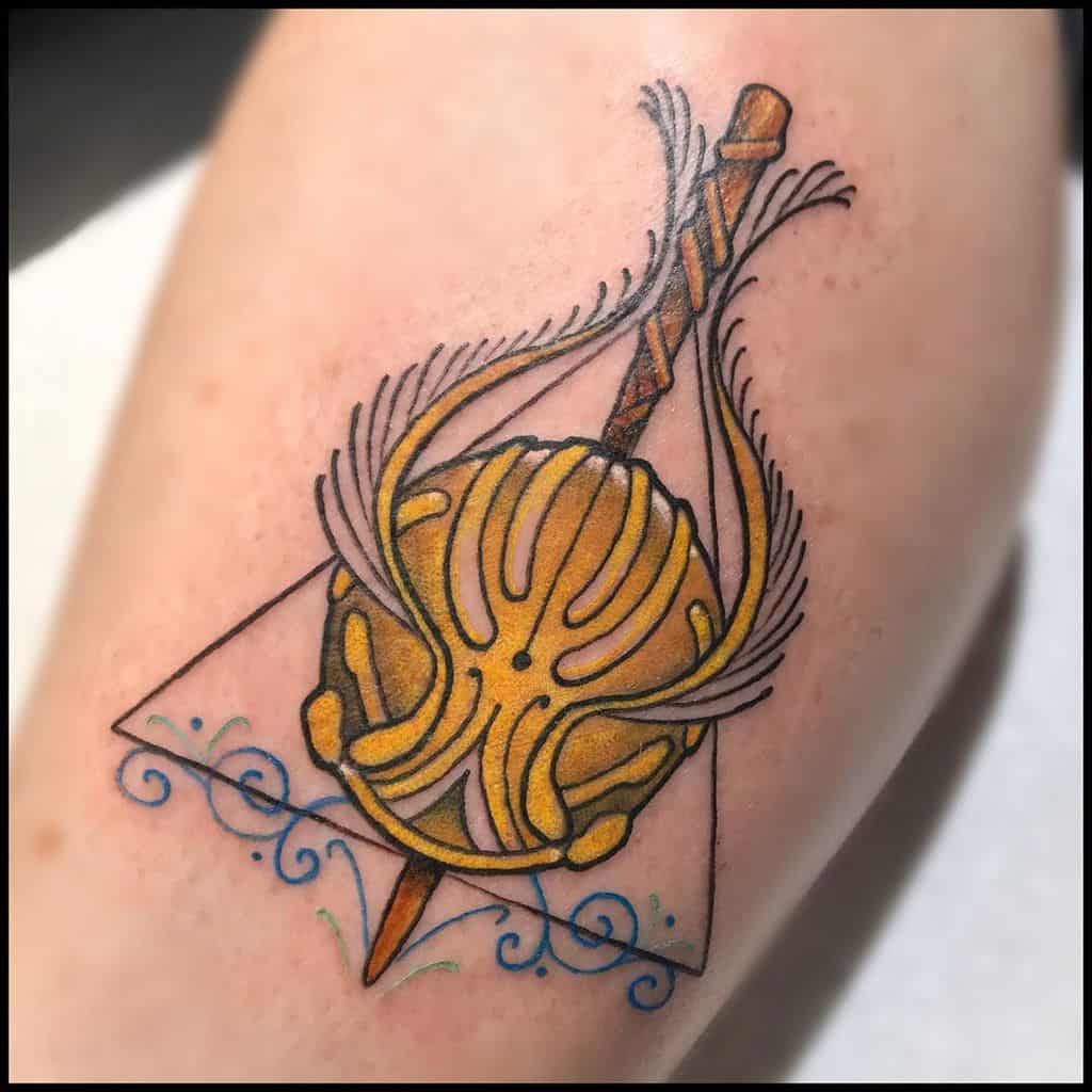 Colorful Deathly Hallows tattoo featuring a Golden Snitch, Elder Wand, and intricate blue swirls for a magical and dynamic design.