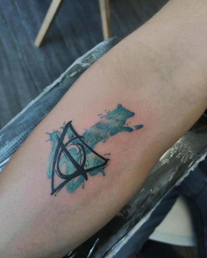 Deathly Hallows tattoo with a blue watercolor wolf Patronus, symbolizing magic, protection, and the connection to Harry Potter’s world