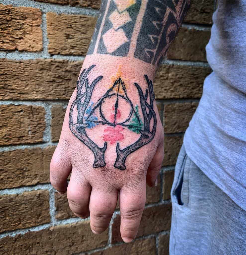 Deathly Hallows tattoo on the hand with watercolor shading and stag antlers, symbolizing Harry Potter’s Patronus and magical legacy