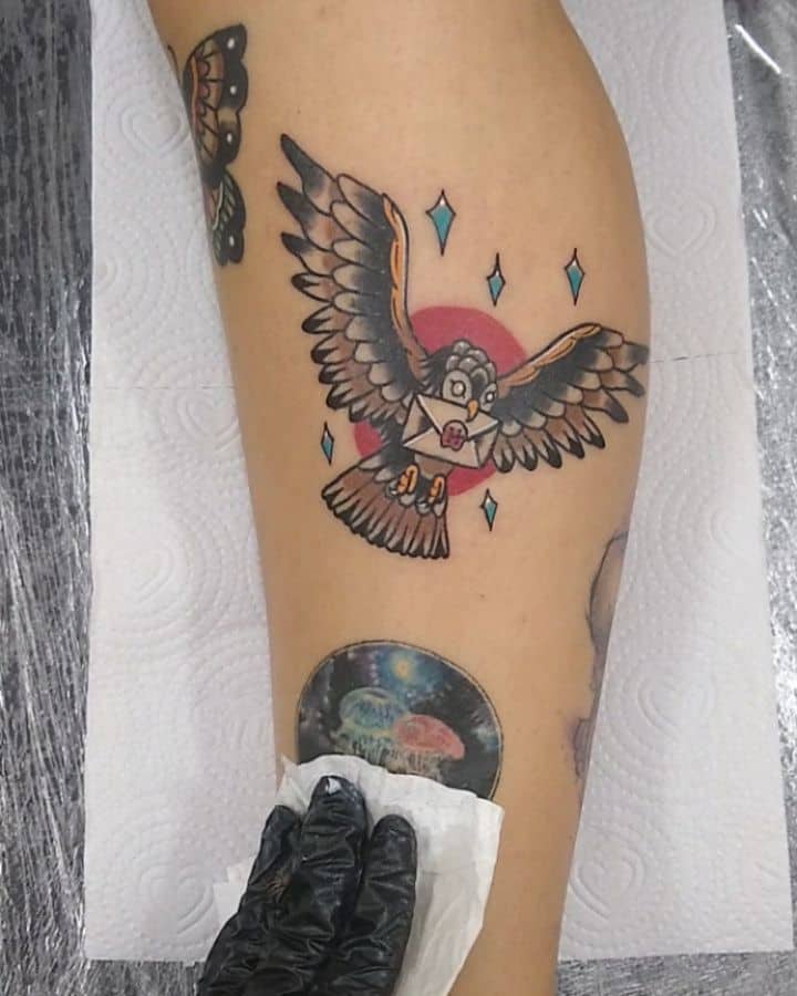 Traditional-style Hedwig tattoo from Harry Potter, featuring the snowy owl delivering a Hogwarts letter with a red sun and sparkling accents