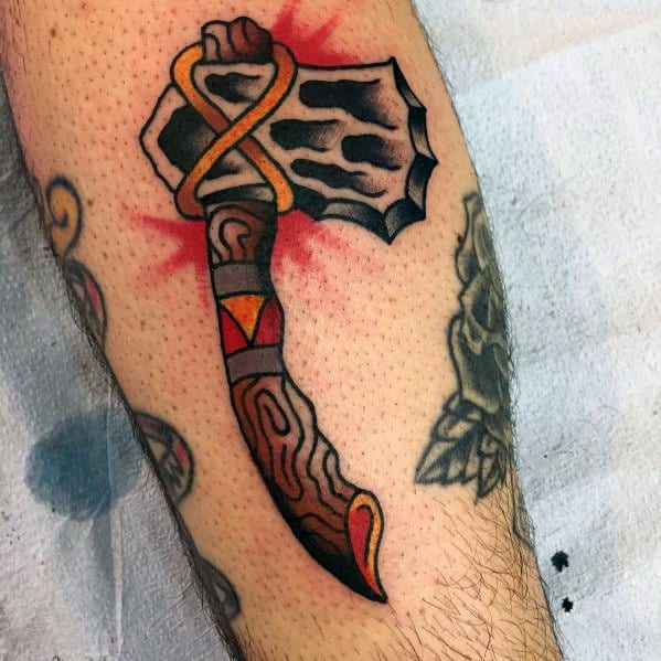 Bold traditional-style hatchet tattoo with a rugged black blade, a wood-textured handle, and golden rope detail, accented with red shading.