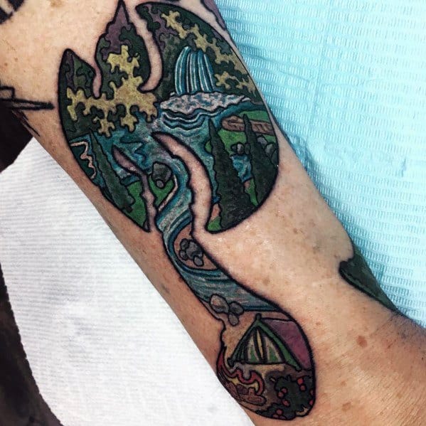 Colorful hatchet tattoo with intricate puzzle piece designs, depicting a nature scene with waterfalls, trees, and a tent, blending surreal and abstract styles.