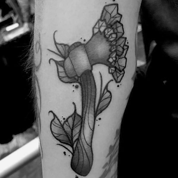 Black and grey hatchet tattoo with a wood-textured handle, surrounded by leaves, and a crystalized blade, blending natural and geometric elements.
