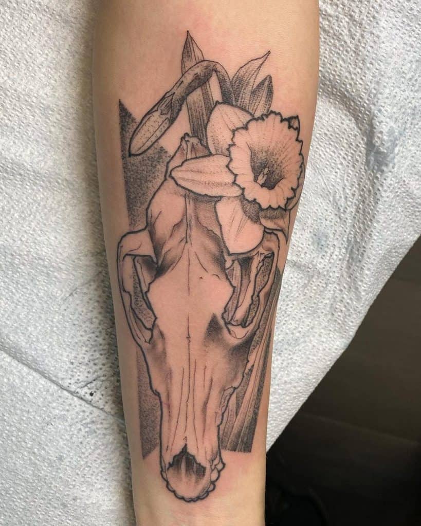 This tattoo beautifully combines a delicate skull with daffodils emerging from it. The fine details and shading give the tattoo an artistic and thoughtful contrast between life and death, with the flowers symbolizing renewal and the skull representing the cycle of life.