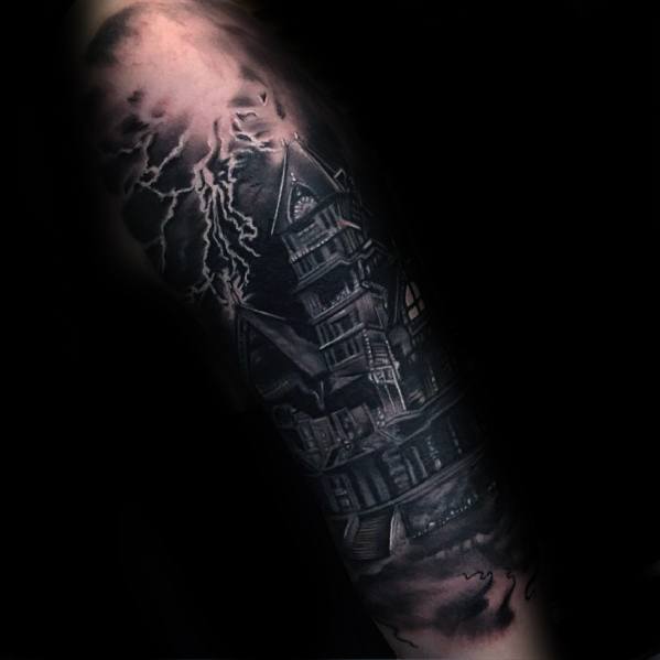 Dark haunted house tattoo on a forearm with lightning bolts, swirling fog, and eerie lighting for a dramatic nighttime horror effect.