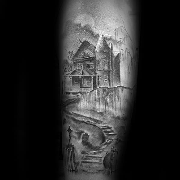 Forearm tattoo of a haunted house on a hill with a winding path, cemetery gates, gravestones, and eerie shadows in a misty setting.