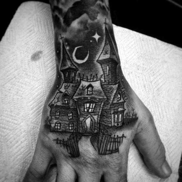 Hand tattoo of a haunted house with pointed towers, crescent moon, stars, dark clouds, and an open gate creating a mystical night scene.