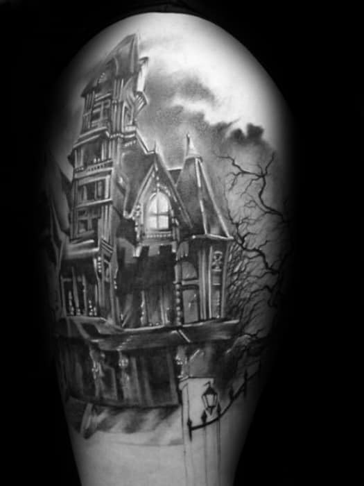 Realistic haunted mansion tattoo on the upper arm with gothic windows, stormy clouds, leafless tree branches, and a wrought-iron gate.