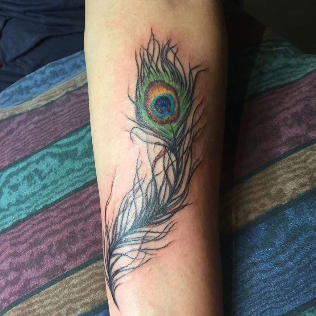 Tattoo of a colorful peacock feather on an arm, featuring vivid blues, greens, and purples with detailed feather strands