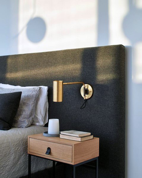Modern bedroom with black upholstered headboard gold wall sconce and wood nightstand.