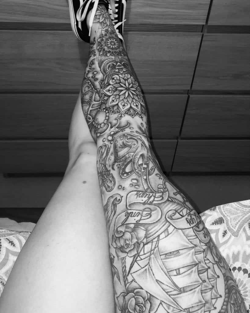 A tattooed leg sleeve featuring a ship, octopus, jellyfish, ocean, pearls flowers, banners with text on it and intricate patterns