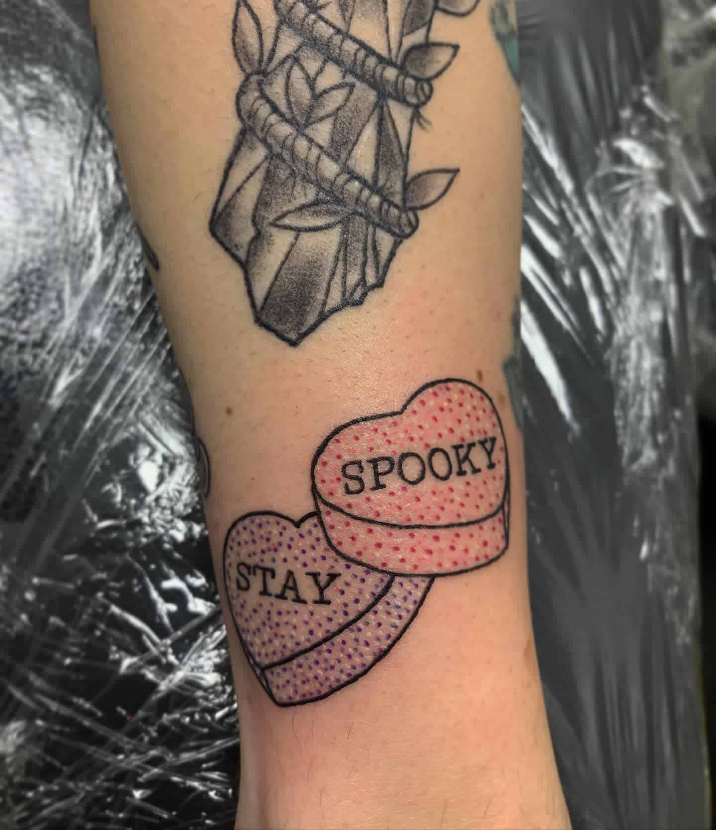 Tattoo of two heart-shaped candies, one says "STAY" and the other "SPOOKY