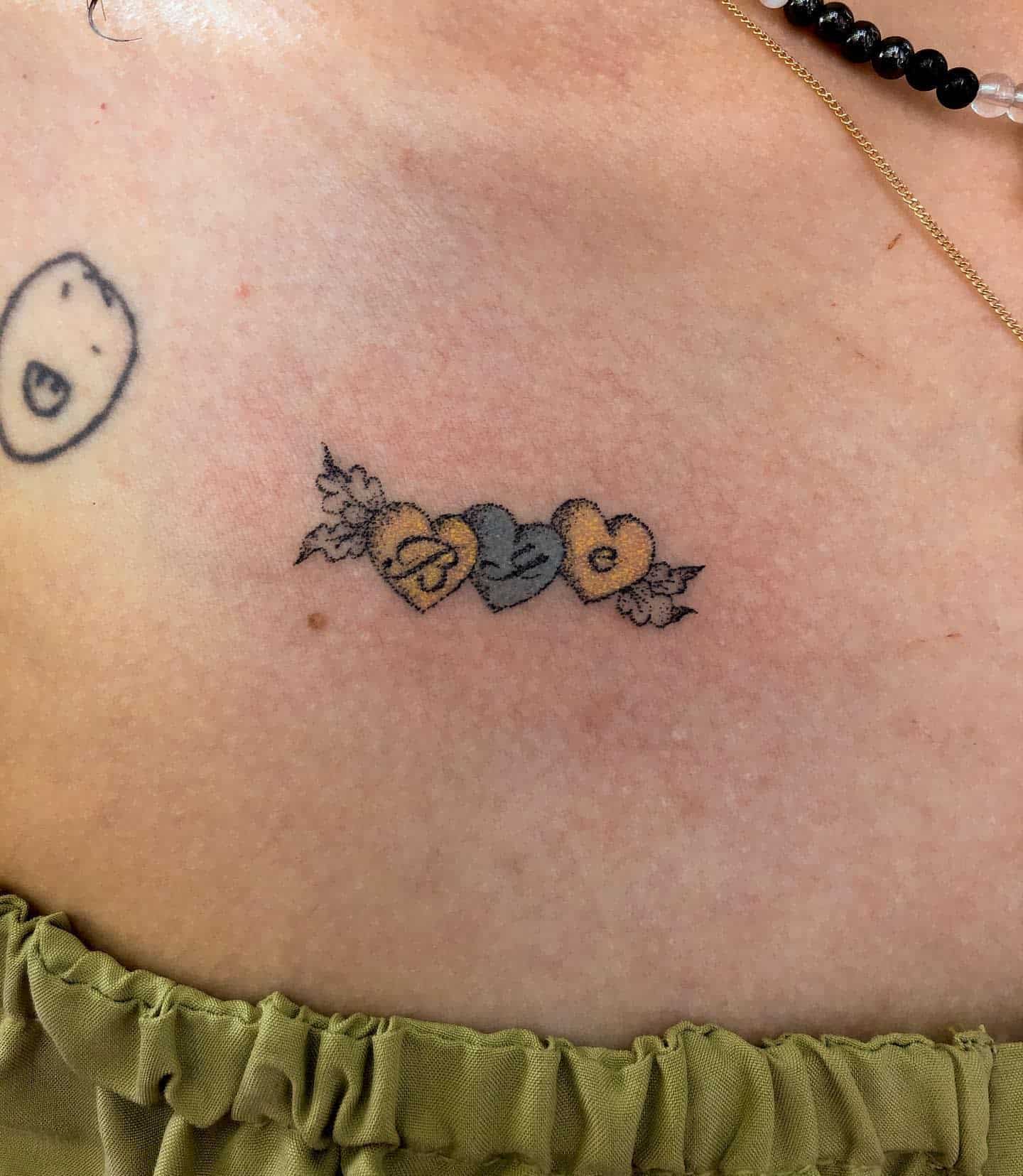 Delicate tattoo of three small hearts with initials "Bye" and floral details