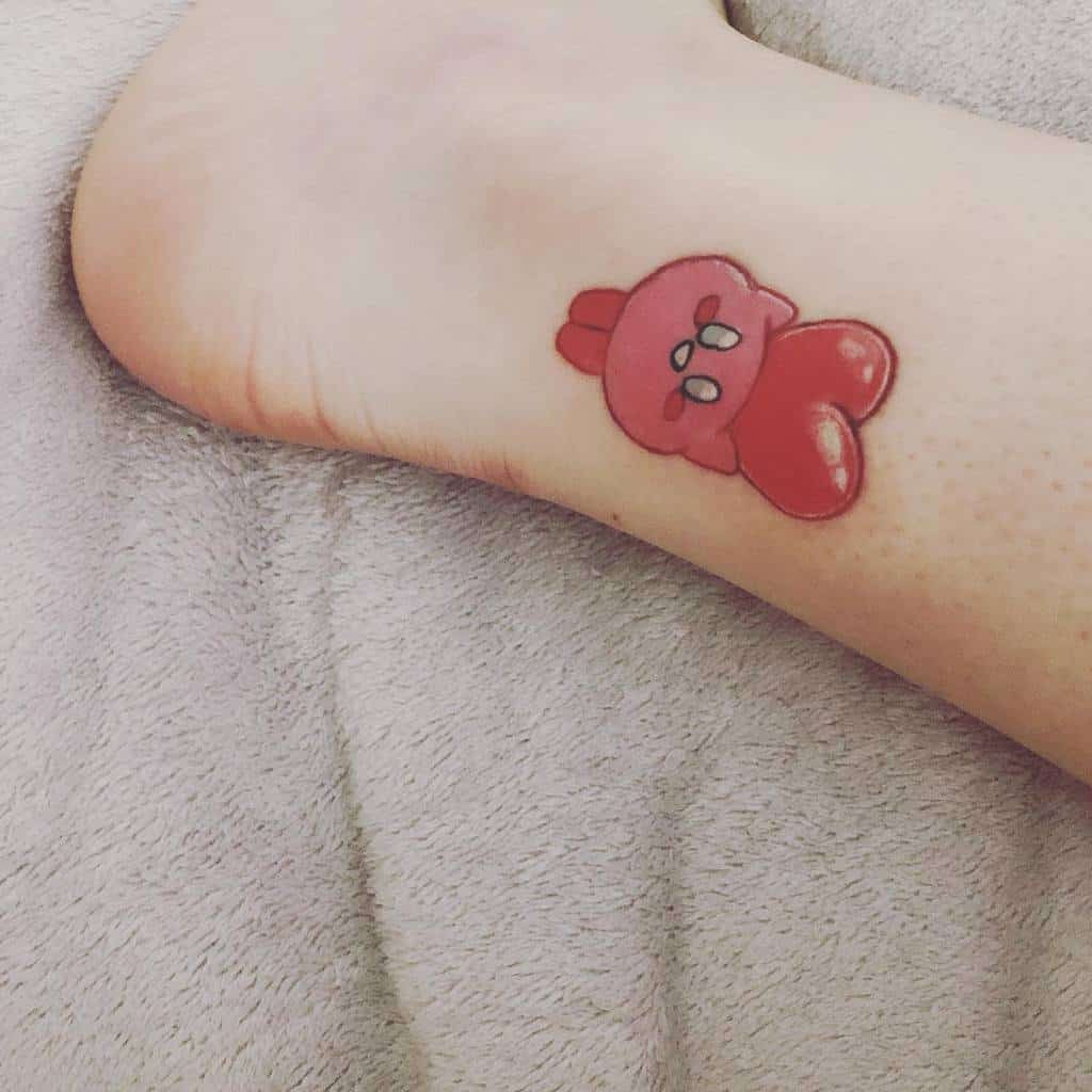 Small Kirby tattoo, designed with a glossy, heart-shaped aesthetic above his head