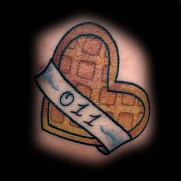 Heart-shaped waffle tattoo with a banner displaying "011," blending a love for breakfast with a subtle pop culture reference in a simple design.