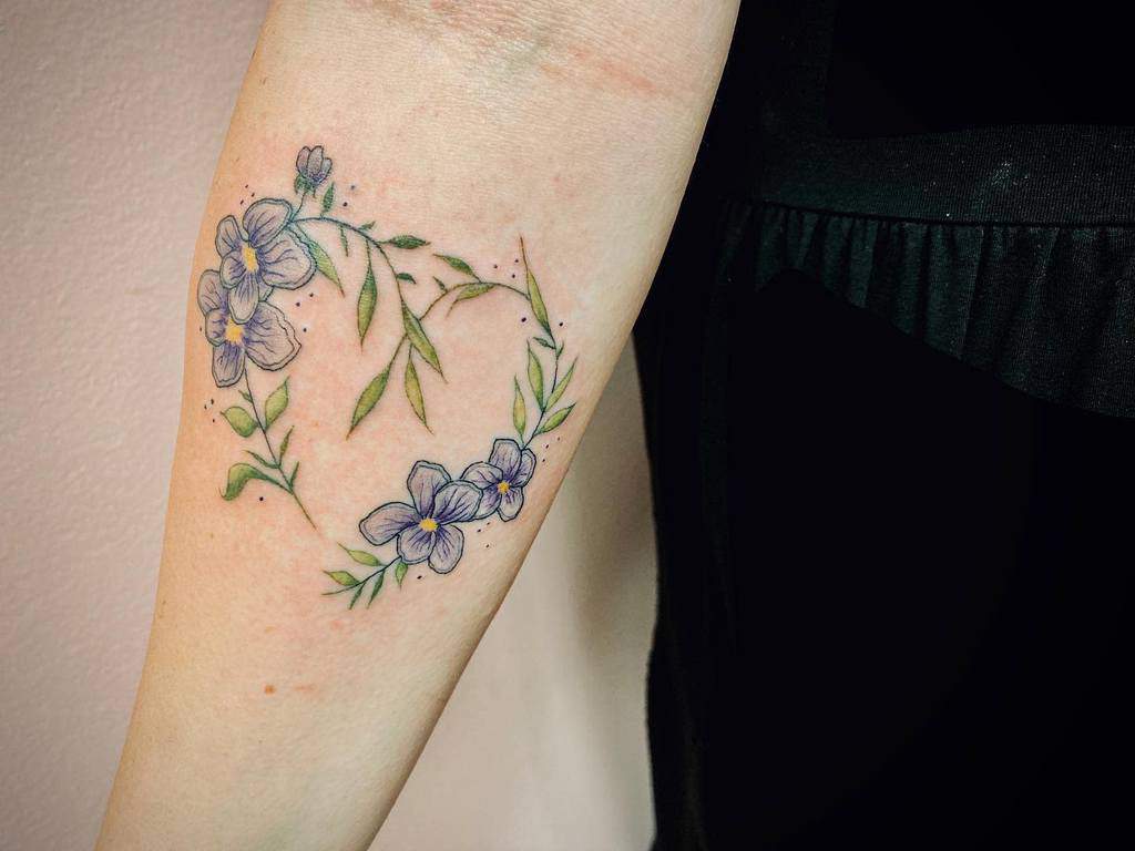 Delicate floral wreath tattoo with soft violet flowers and green leaves, forming a graceful and nature-inspired design