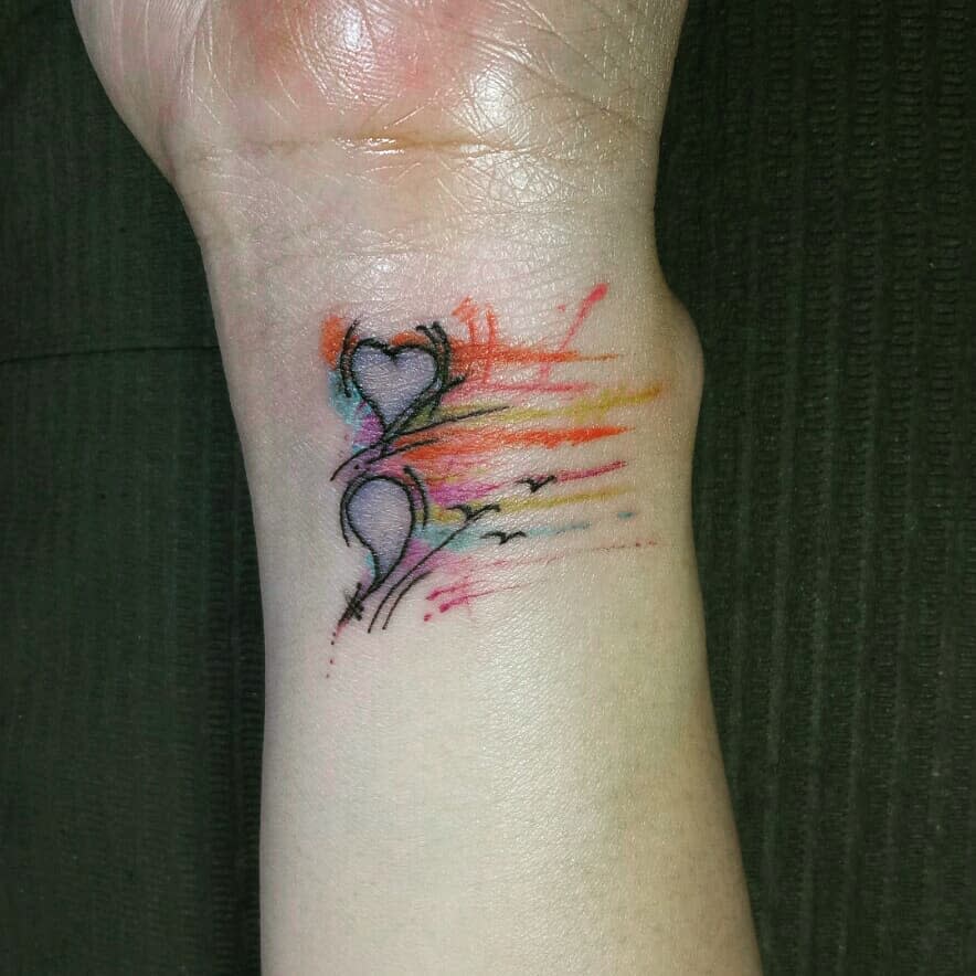 This tattoo features a combination of two hearts, represented in a minimalist style, with abstract strokes of vibrant watercolor splashes. The inclusion of the semicolon at the end subtly ties into the theme of mental health and resilience, with the flowing lines symbolizing freedom and emotional release.