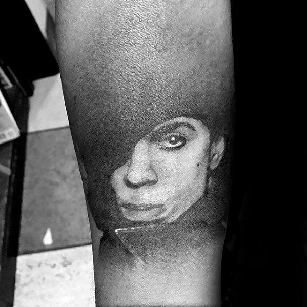 Black and white tattoo of Prince's face shaded in ink on forearm