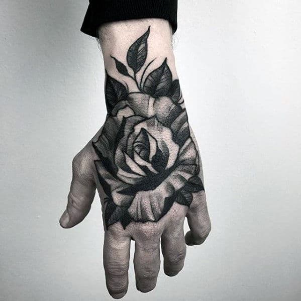 Black rose tattoo covering the back of a person's hand, extending from the wrist to the fingers