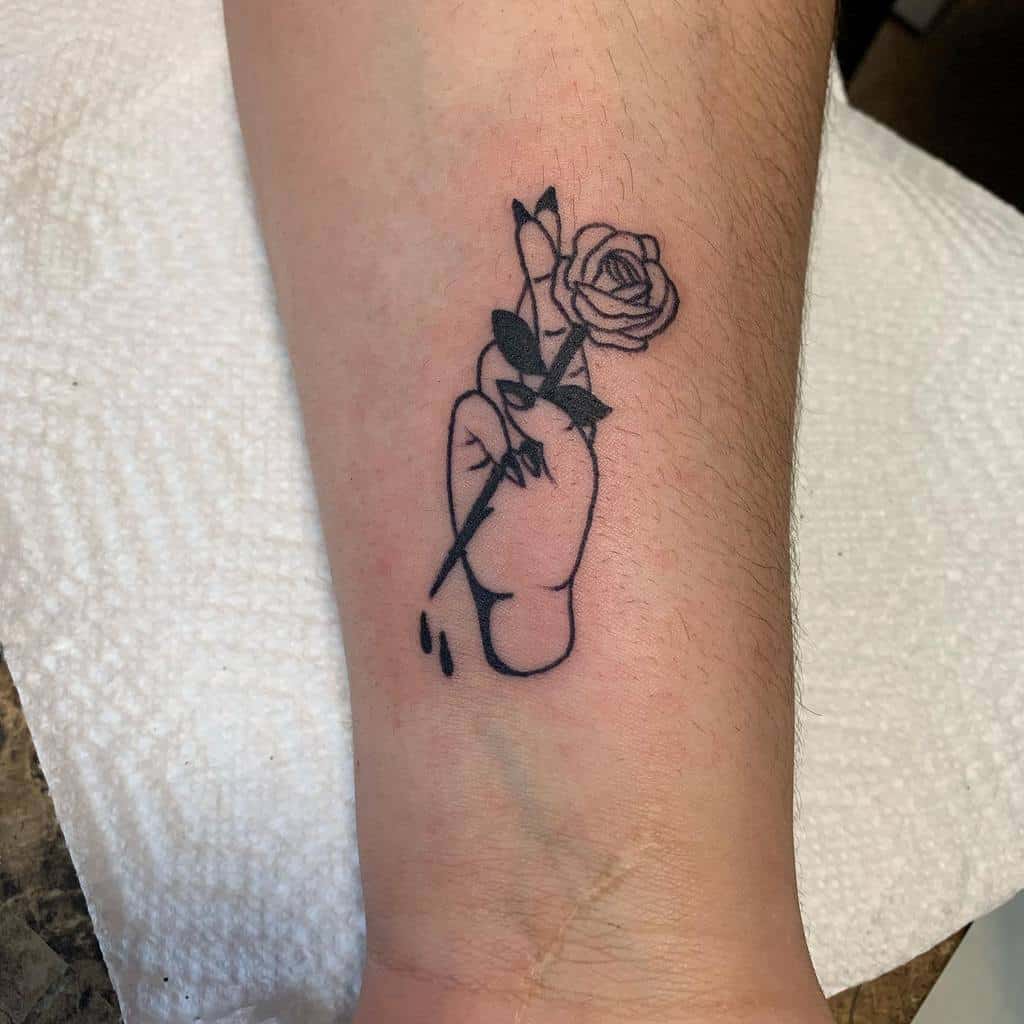 Black line tattoo of a hand holding a thorny rose, with small drops of blood