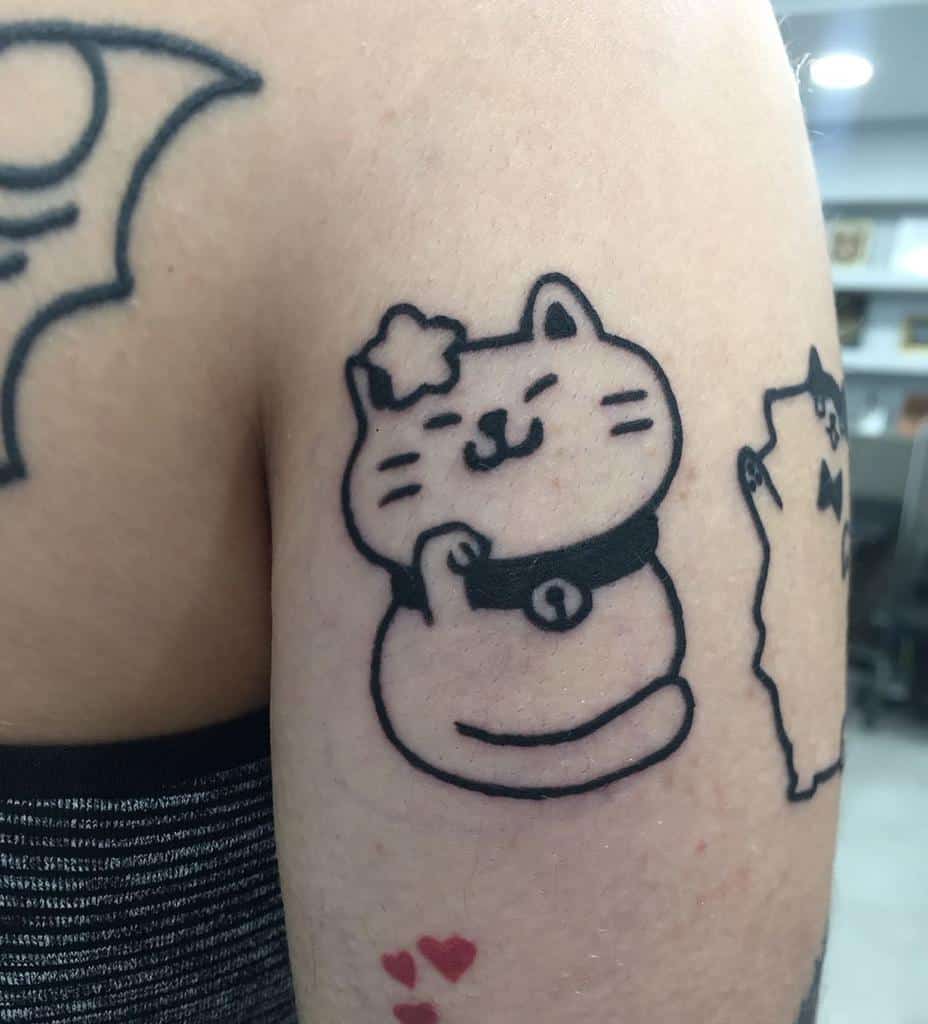 Bold black ink tattoo of a cute, chubby lucky cat with a smiling face, a collar with a bell, and a small star on its head