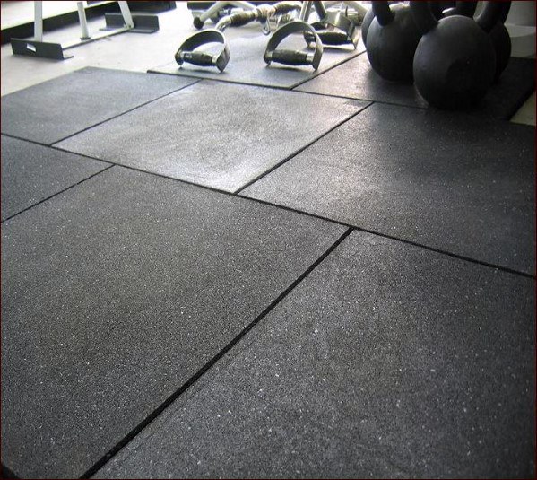 Close-up of durable black rubber flooring with gym equipment like kettlebells in the background.