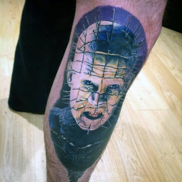 Realistic *Hellraiser* tattoo of Pinhead with detailed pin grid, eerie shading, and a blue-toned background for a dramatic, haunting look.