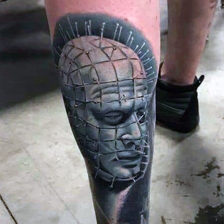 Realistic *Hellraiser* tattoo of Pinhead with detailed pin grid, smooth shading, and a cold, eerie expression for a haunting leg piece.