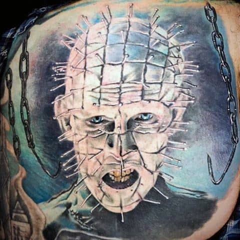 Color *Hellraiser* tattoo of Pinhead with piercing blue eyes, detailed pin grid, eerie shading, and hanging chains for a dark, menacing effect.