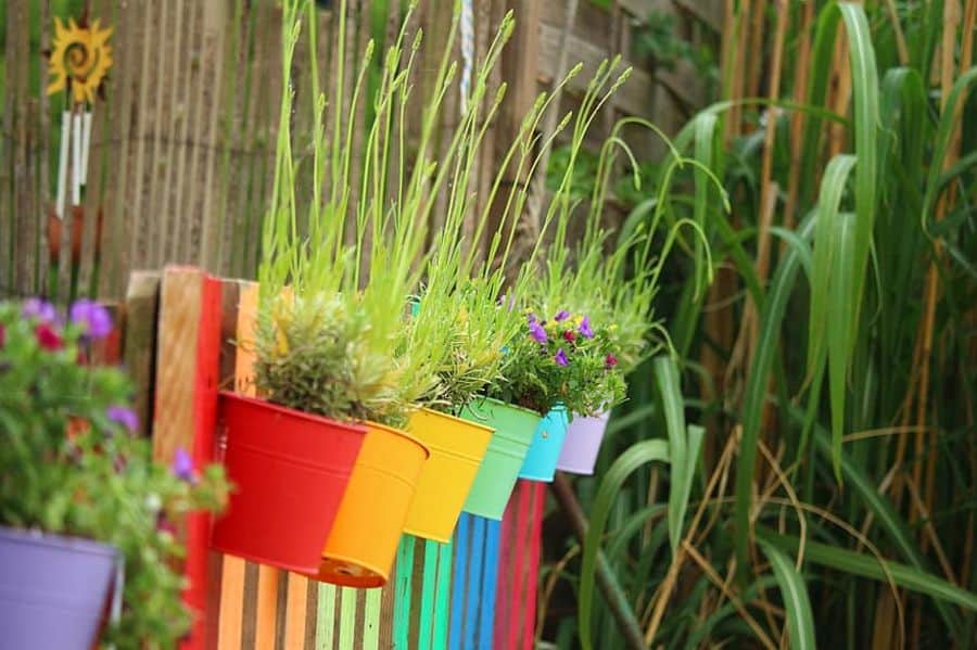 Vibrant multi-colored pots with plants hang on a wooden fence in a lush garden setting