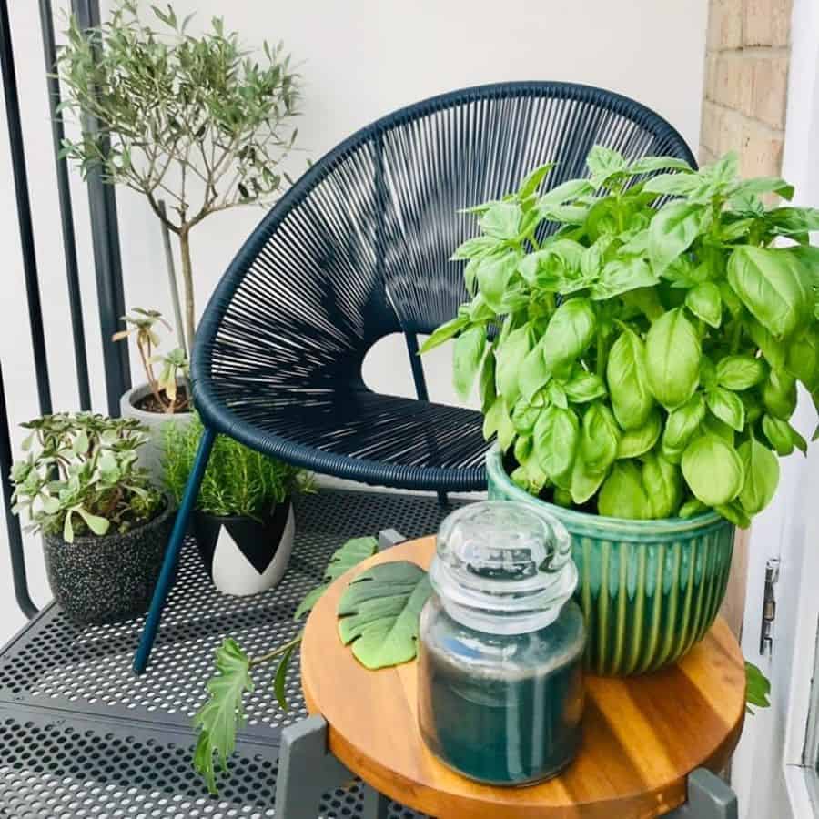 Balcony with potted herbs, a black chair, and a small wooden side table with a candle.