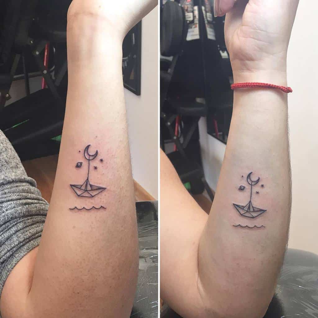 Matching minimalist tattoos featuring a paper boat floating on waves with a crescent moon, Saturn and stars above