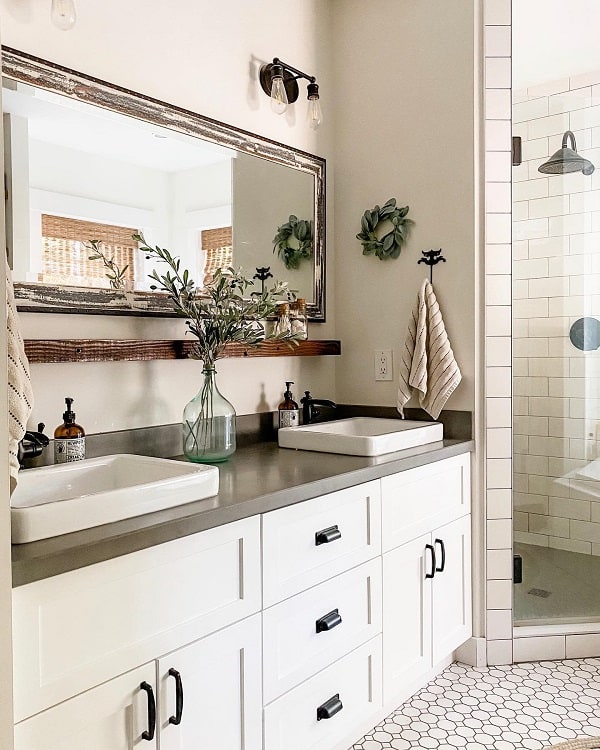 Modern farmhouse bathroom with double sinks, hexagonal floor tiles, a glass shower, and decor including plants and towels