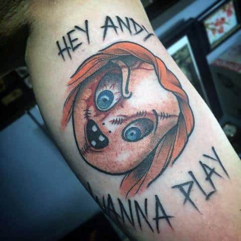 Chucky tattoo featuring his stitched face in a circular design with bright blue eyes and the phrases "Hey Andy" and "Wanna Play?" for a bold look.