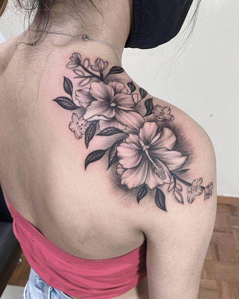 A woman flaunts a striking black and gray hibiscus tattoo that gracefully adorns her shoulder