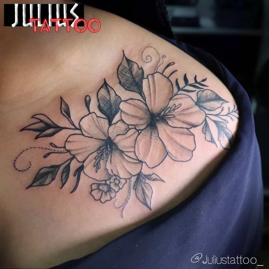 A stunning black and gray hibiscus tattoo elegantly sprawls across the shoulder, its intricate leaves adding a touch of nature's grace