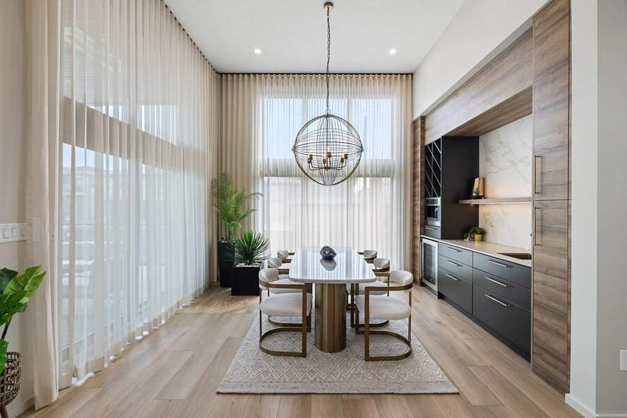 Modern dining room with high-ceiling sheer curtains, a statement chandelier, and sleek furnishings.