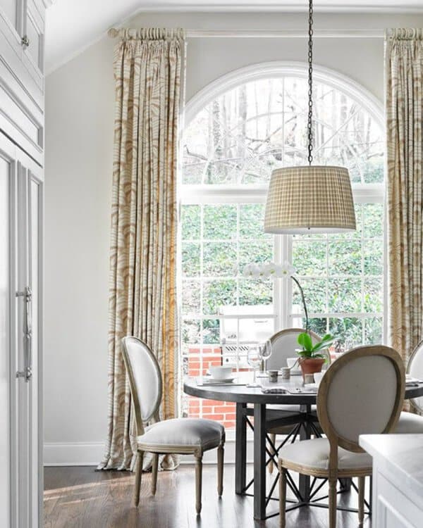 Bright dining room with high ceilings, patterned curtains, arched windows, and elegant seating.