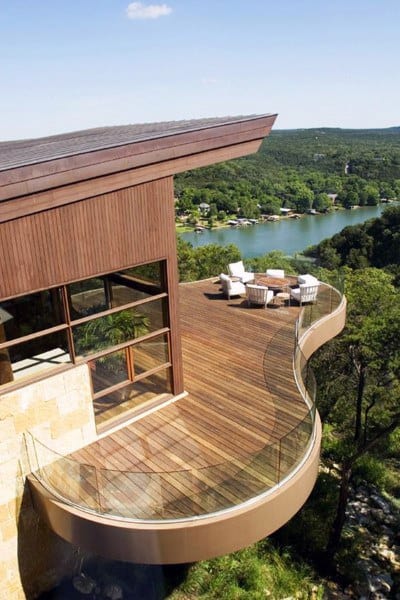 Curved wooden balcony deck with glass railing and panoramic lake views.