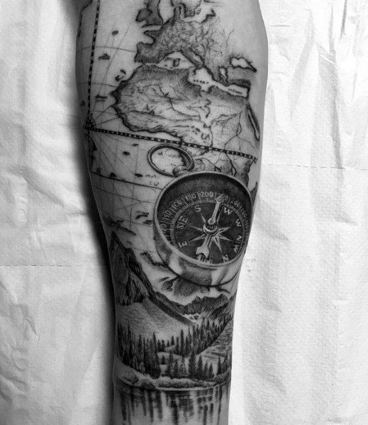 Detailed travel-themed tattoo featuring a world map, compass, and mountain landscape, symbolizing adventure and exploration.