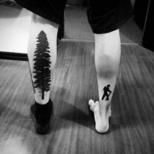 Minimalist leg tattoos featuring a tall pine tree on one calf and a hiker silhouette on the other, symbolizing nature and adventure.