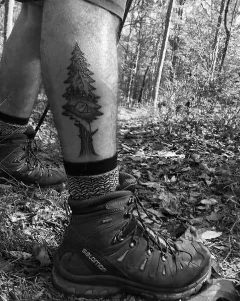 This tattoo features a treehouse nestled within tall pines, symbolizing adventure and a love for nature, placed on the lower leg.
