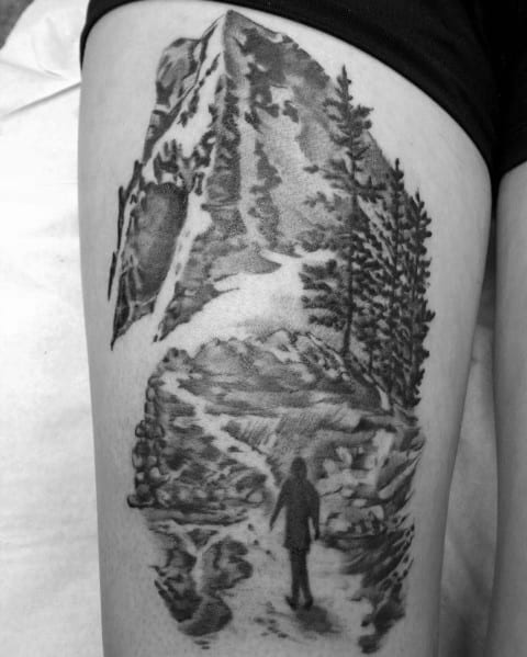 A black and gray tattoo of a hiker on a winding mountain trail, surrounded by trees and towering peaks, symbolizing adventure and exploration.