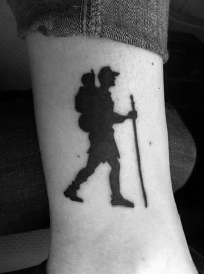 This tattoo depicts a silhouette of a hiker carrying a child in a backpack, symbolizing adventure, exploration, and a love for the outdoors.
