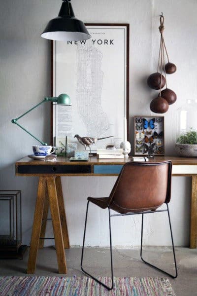 Stylish desk with a map, books, green lamp, decor items, and a brown chair in a cozy, well-lit workspace