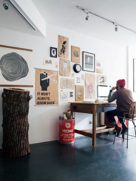 Person sitting at a desk in a room with various wall art and a tree stump as decor