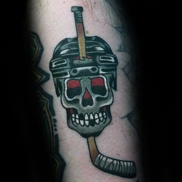 Bold traditional-style tattoo of a skull wearing a hockey helmet with a hockey stick through the top, symbolizing toughness and love for the game.