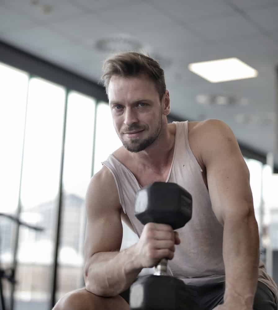 smiling man in tank top holding black dumbbell in gym