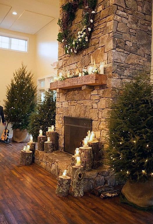 Holiday-themed stone fireplace with wood accents, candles, and decorated evergreen trees.
