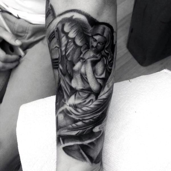 Black and white angel tattoo on someone's forearm, with hands in a prayer position